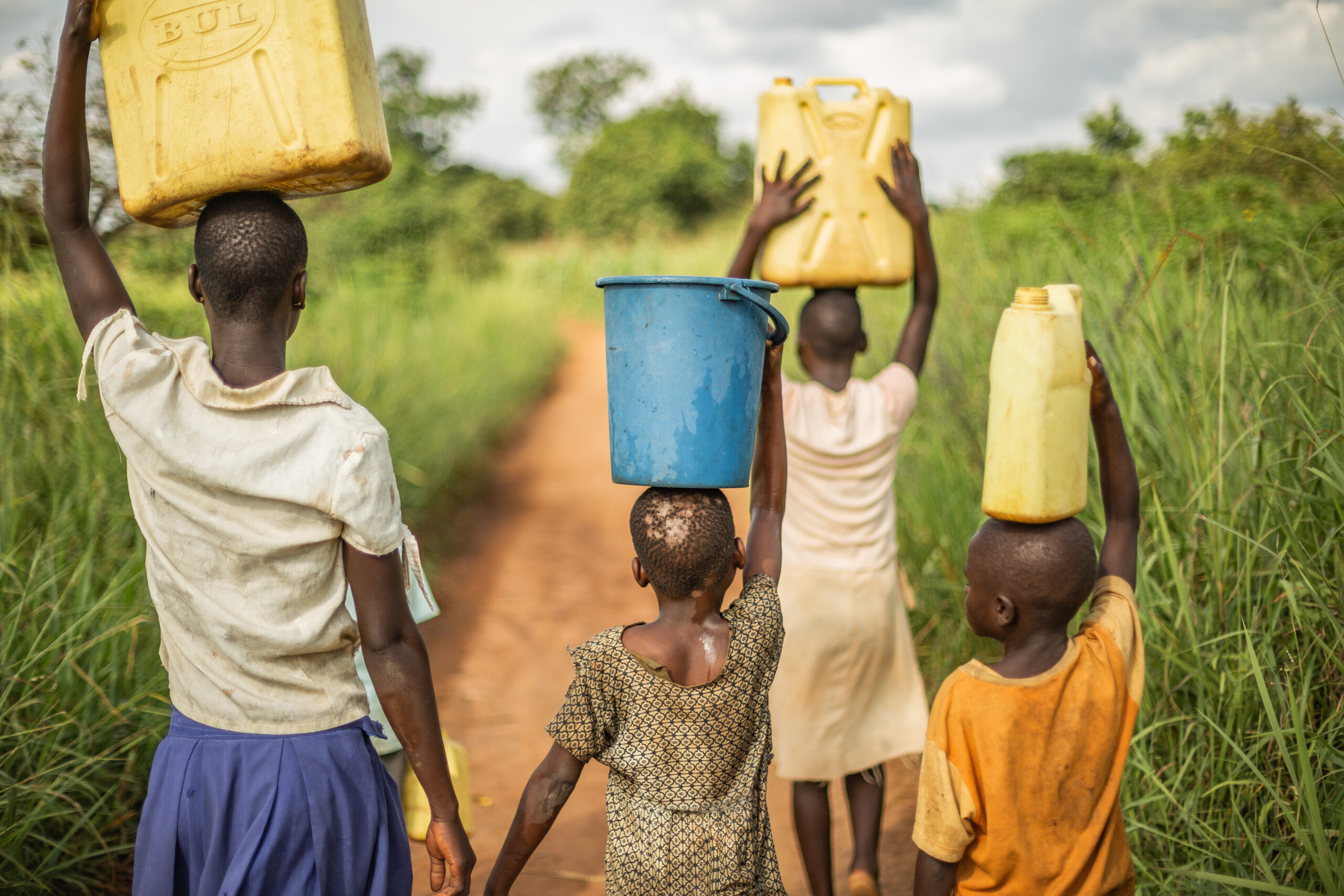 Group if young African kids walking with buckets and jerrycans on their head as they prepare to bring clean water back to their village.