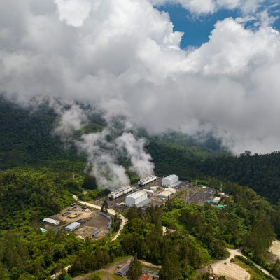 Mountain forest with Geothermal station with steam and pipes. Renewable energy production at a power station. Mindanao, Philippines. Aerial drone shot.