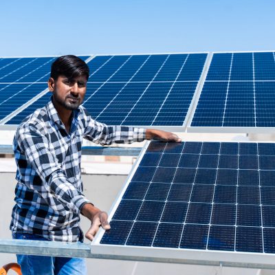 Portrait of Indian worker installing solar panels on roof of house. Maintenance of photovoltaic panel system. Concept of alternative, renewable energy.